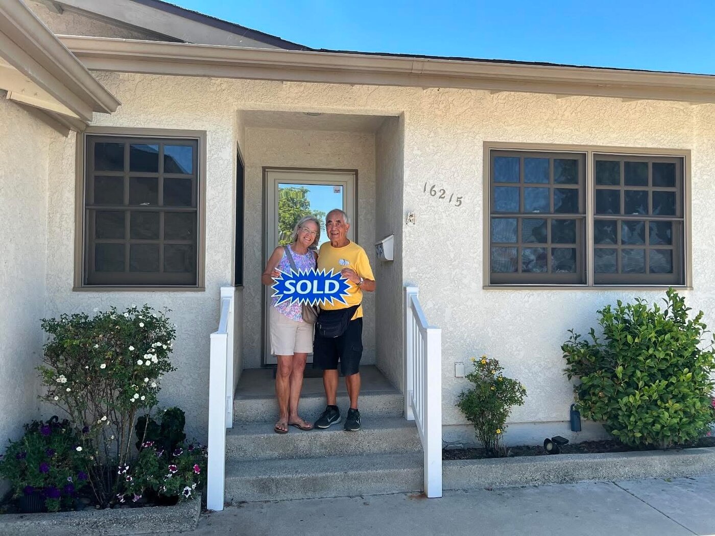 The Tsuruis holding a Sold sign on the porch of their new Torrance home